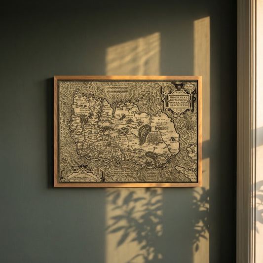 Hiberniae, Britannicae Insvlae nova descripto Ireland map framed print in a natural oak frame on a dark green wall beside a window, dappled plant shadow