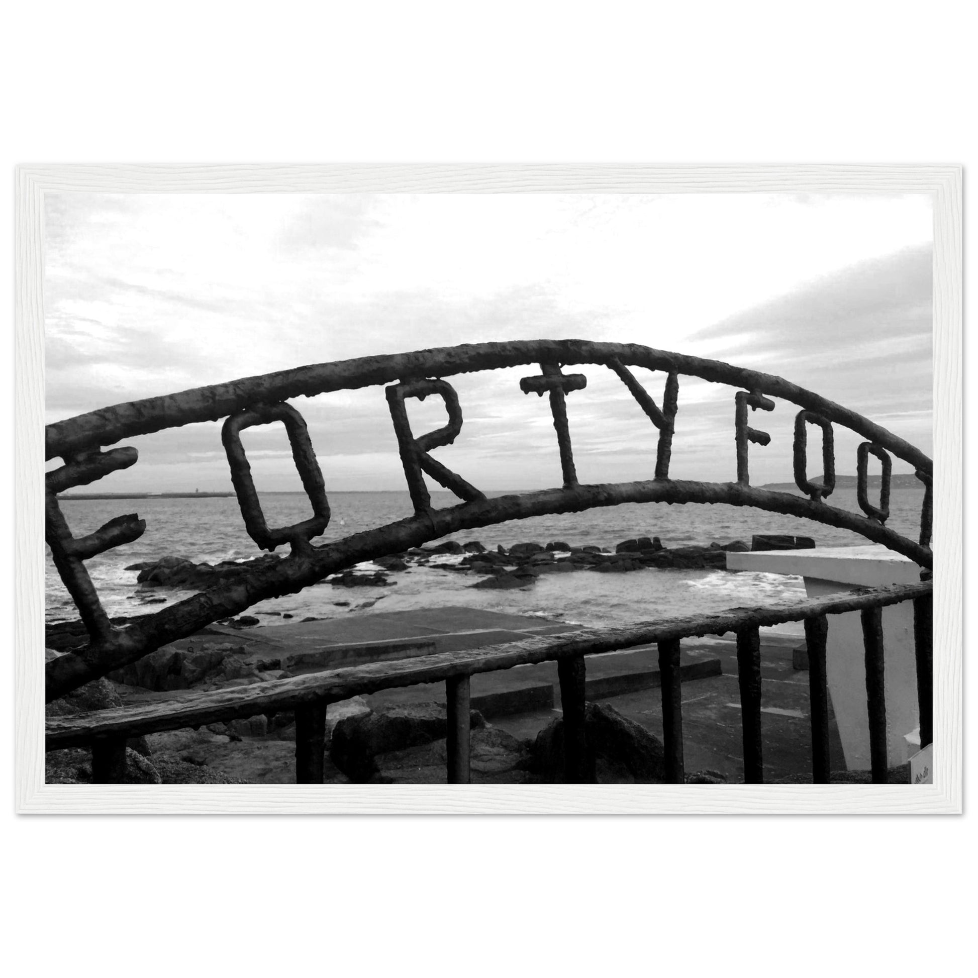 Monochrome seascape photo capturing the serene beauty of the Forty Foot bathing spot in Dublin, Ireland. Martello tower stands in the distance against a clear sky.