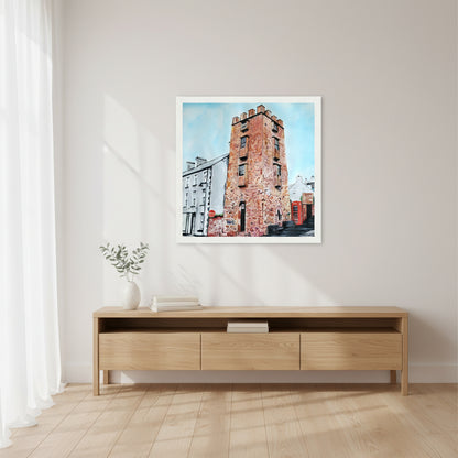 30×30 cm white-framed square art print of The Curfew Tower Cushendall displayed above a console table, bright airy interior, soft white walls, light oak furniture, calm atmosphere, lifestyle home photograph with gentle natural lighting.
