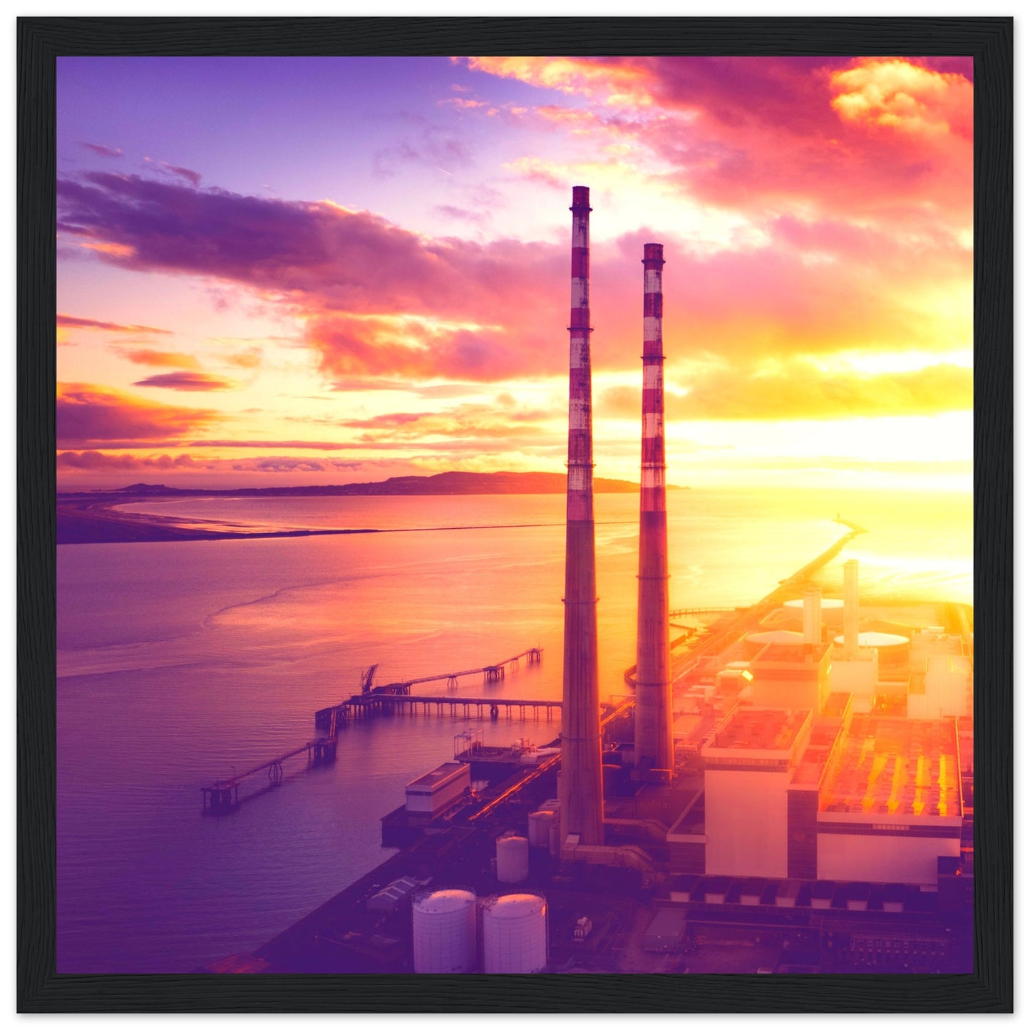 A framed print of Dublin's industrial landscape, featuring the iconic Poolbeg Towers and Lighthouse at sunrise. This aerial view captures the blend of industrial structures with a serene, sunlit horizon, showcasing the harmony between technology and nature. Perfect for admirers of drone photography, industrial architecture, and Ireland's coastal beauty.