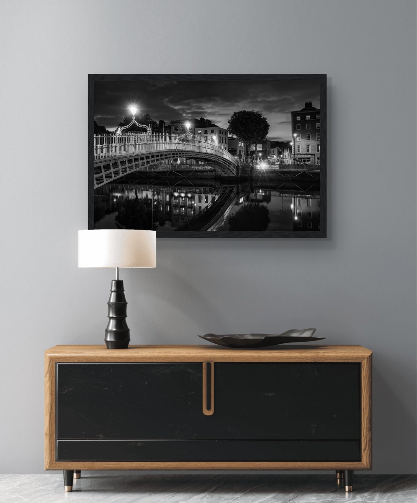 Black and white framed wall art print of Ha'penny Bridge in Dublin, Ireland at night. The iconic bridge is beautifully illuminated, with reflections shimmering in the River Liffey. Elegant, high-quality print adds a touch of sophistication and historical charm to any decor.