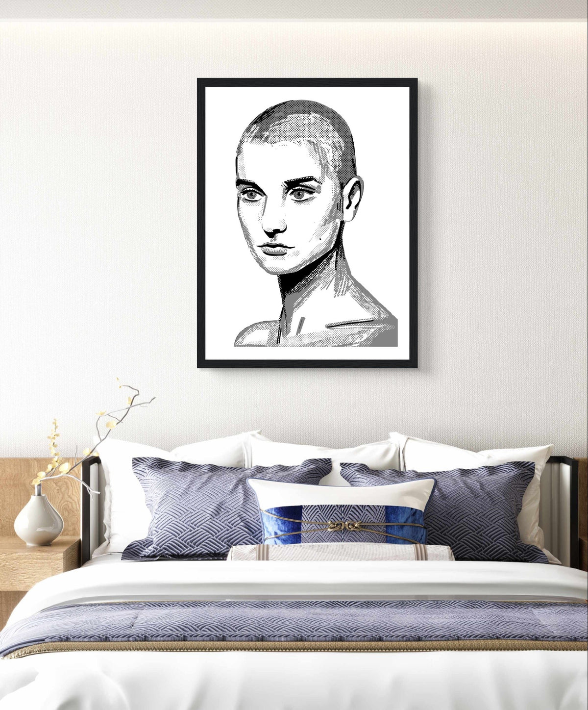 Sinéad O'Connor black and white line portrait print in a black frame above a bed with blue cushions