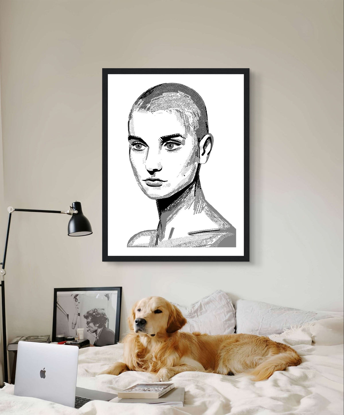Sinéad O'Connor black and white line portrait print in a black frame above a bed with a golden retriever