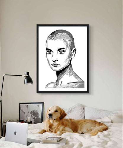 Sinéad O'Connor black and white line portrait print in a black frame above a bed with a golden retriever