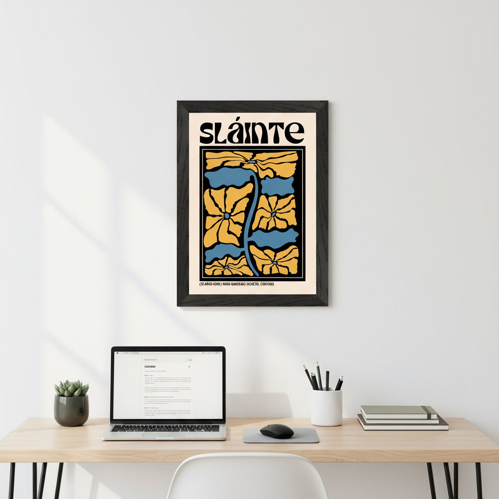 Sláinte print framed and placed above a tidy desk setup with plants, stationery, and a laptop. Clean modern interior, editorial style.