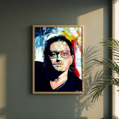 Vibrant Bono U2 framed print in a natural oak frame on a dark green wall beside a window, dappled plant shadow