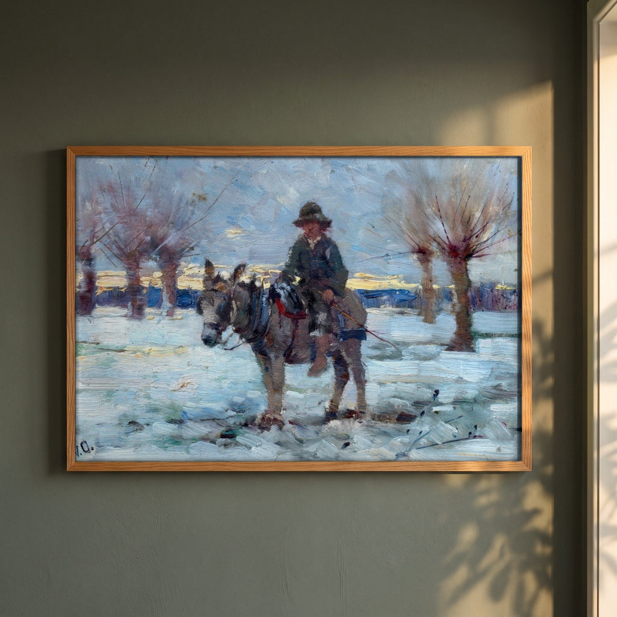 Boy on a Donkey in a Snowy Landscape by Walter Osborne framed print in a natural oak frame on a dark green wall beside a window, dappled plant shadow
