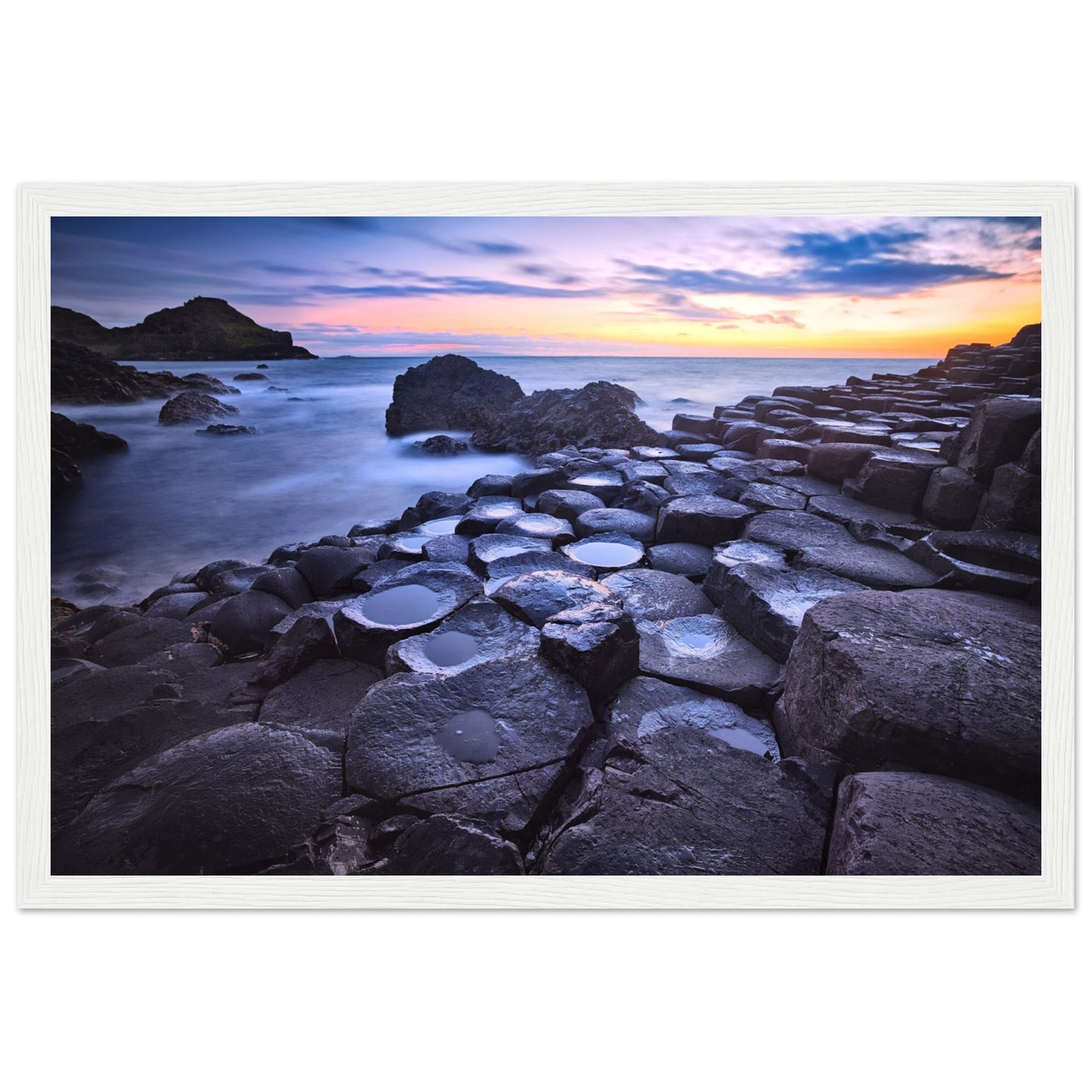 Framed art print of a breathtaking sunset at Giant's Causeway. Features iconic basalt columns against a warm, colorful sky. Perfect for adding sophistication and natural beauty to any home or office decor. Ideal for nature and art enthusiasts.