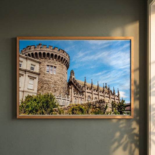 Dublin Castle photographic print in a natural oak frame on a dark green wall beside a window, dappled plant shadow