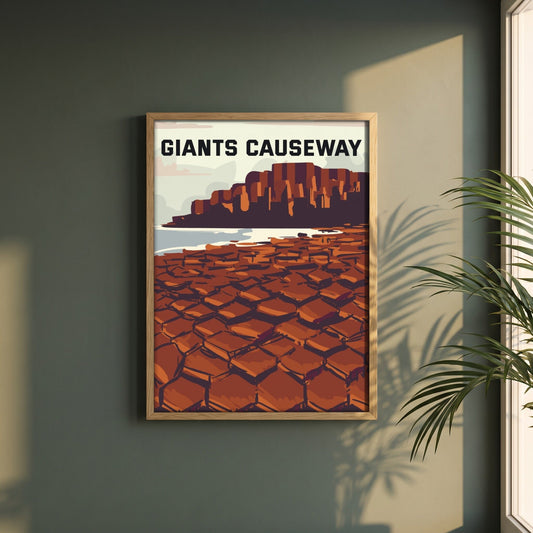 Giant's Causeway retro travel poster in a natural oak frame on a dark green wall beside a window, dappled plant shadow