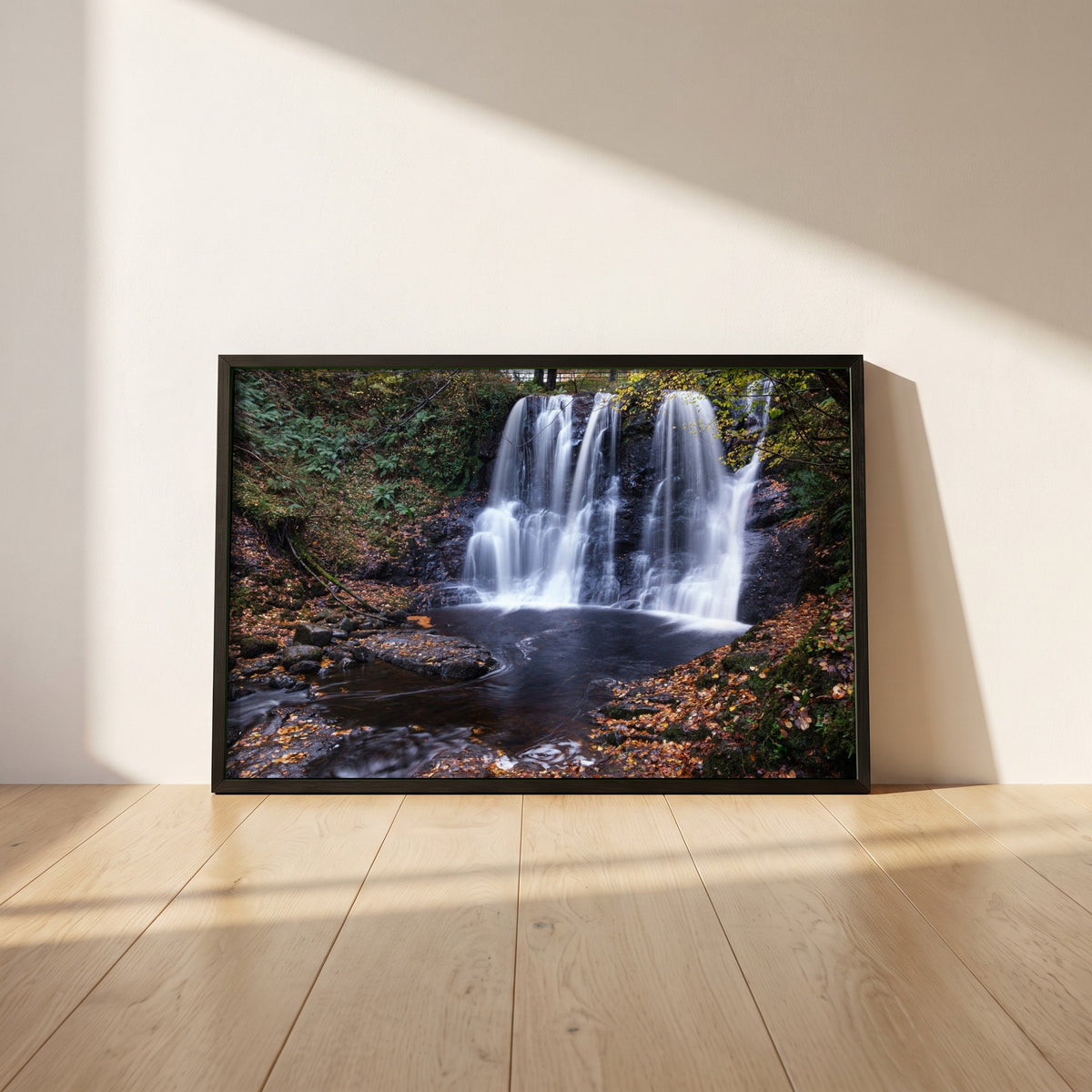 Glenariff Waterfall framed print in a black frame leaning against a white plaster wall on oak floorboards in morning light
