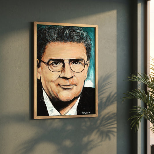 John Hume framed print in a natural oak frame on a dark green wall beside a window, dappled plant shadow