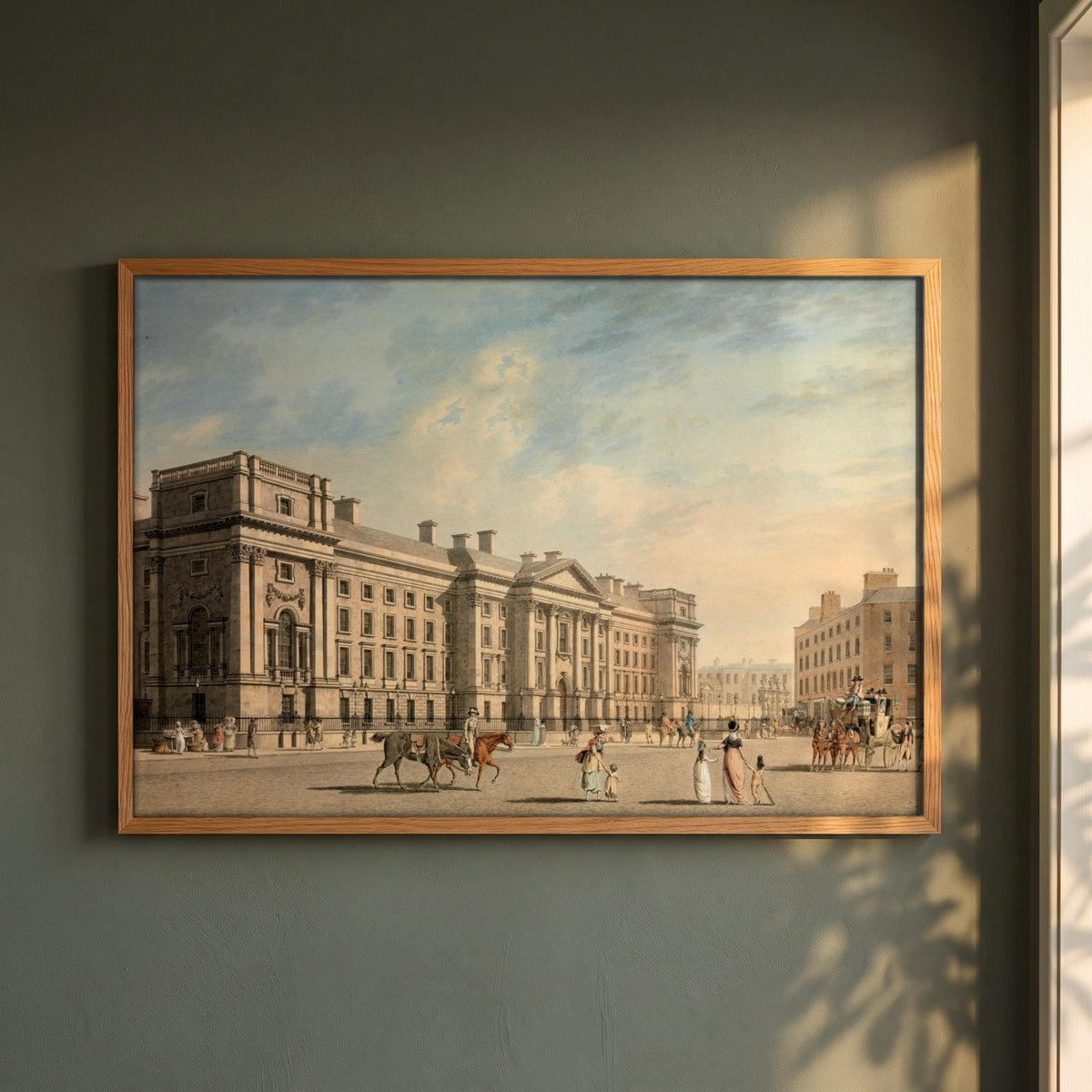 Trinity College, College Green by James Malton framed print in a natural oak frame on a dark green wall beside a window, dappled plant shadow